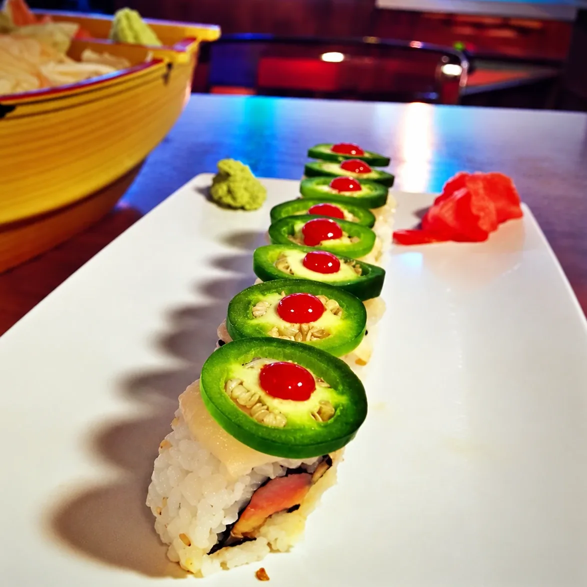 A roll topped with jalapeno and sriracha